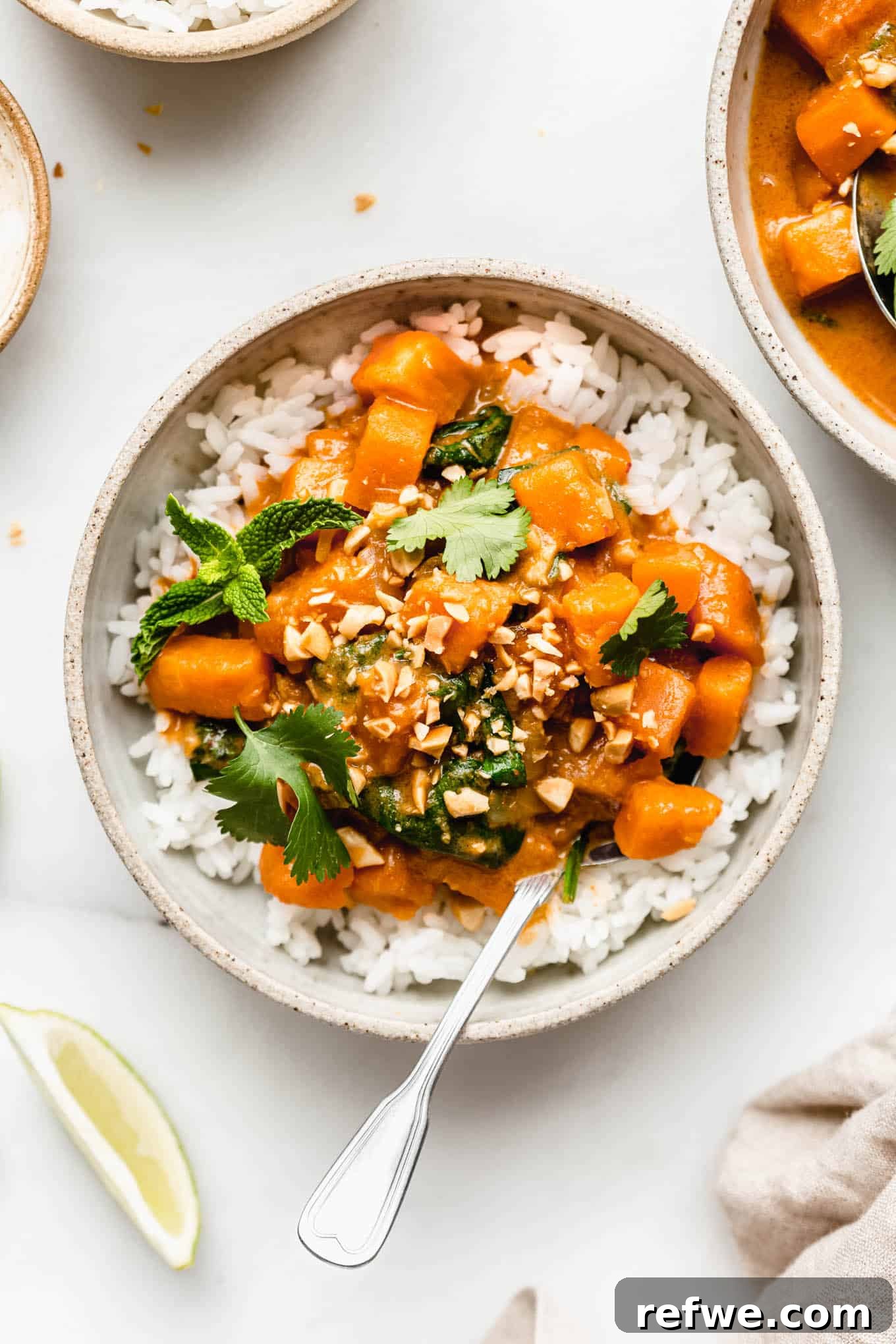 A vibrant bowl of sweet potato curry served over fluffy rice, garnished with crunchy crushed peanuts and fresh cilantro