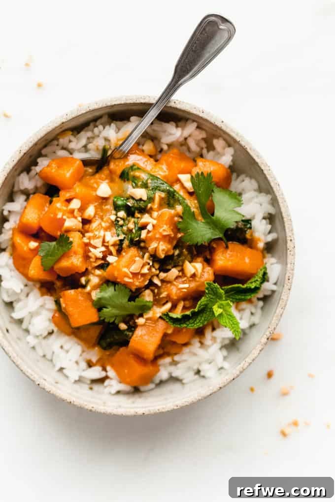 A beautifully presented bowl of sweet potato curry over rice, garnished generously with fresh cilantro and a sprig of mint, ready for enjoyment