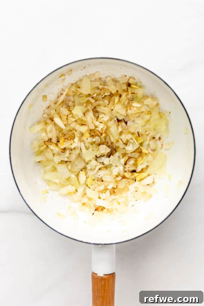 Finely chopped onions and minced garlic gently sautéing in a white pot, emitting fragrant steam