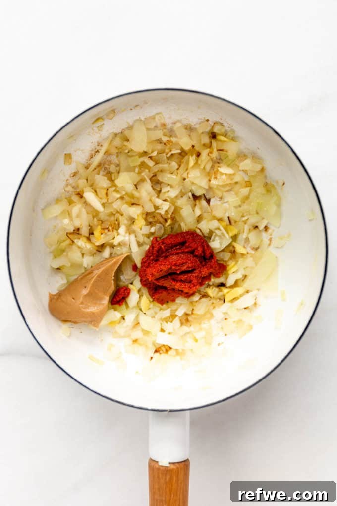 The aromatic blend of sautéed onions, garlic, and ginger, now combined with rich red curry paste and creamy peanut butter, all mixing in a white pot
