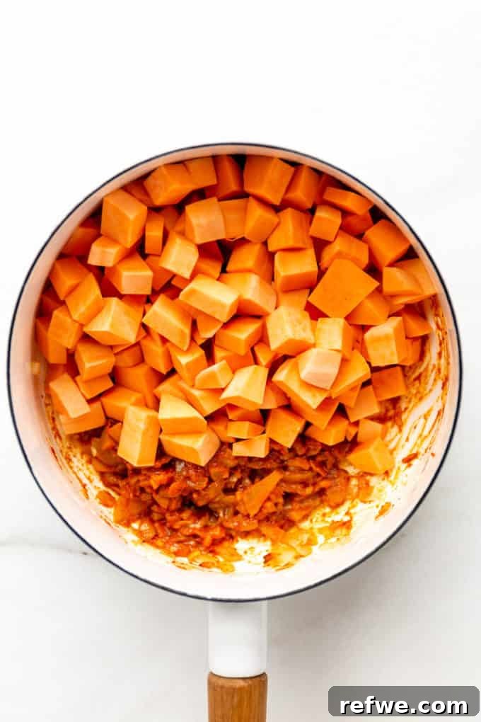 Cubed sweet potatoes, glistening with the vibrant red curry paste, ready to simmer in a white pot