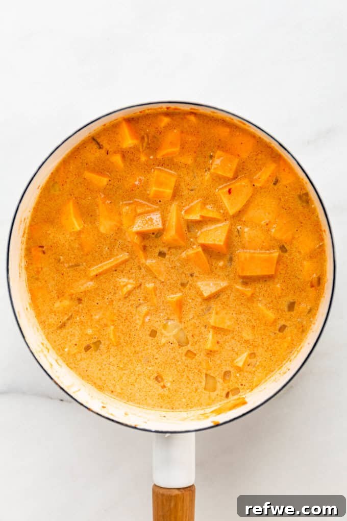 The uncooked sweet potato curry mixture, with creamy coconut milk and broth, ready to simmer in a white pot