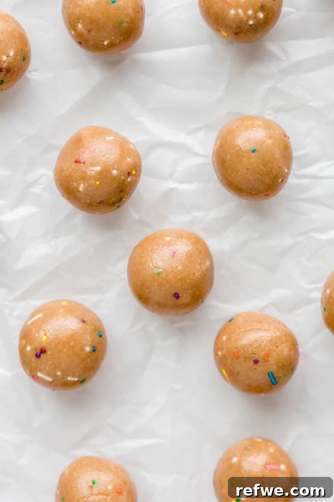 Funfetti Protein Bites 12 Rows of freshly made Birthday Cake Protein Balls resting on parchment paper, awaiting their chilling period.