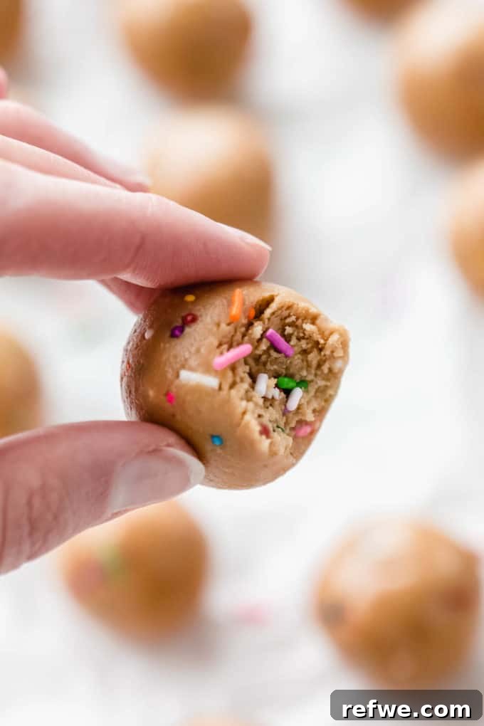 Funfetti Protein Bites 13 A hand holding a partially eaten Birthday Cake Protein Ball, revealing its vibrant, sprinkle-filled interior and soft texture.