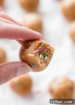 A hand holding a protein ball with a bite taken out of it, revealing a sprinkle-filled interior.