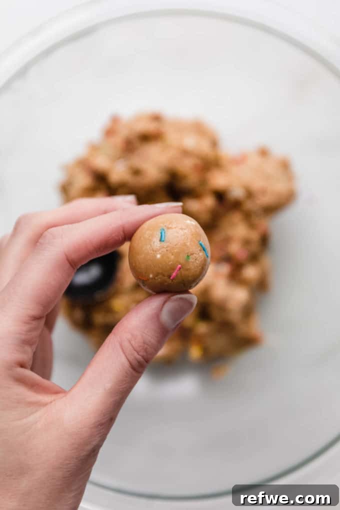 Funfetti Protein Bites 10 A hand gently holding a freshly rolled birthday cake protein ball, showcasing its perfectly round shape and sprinkle details.