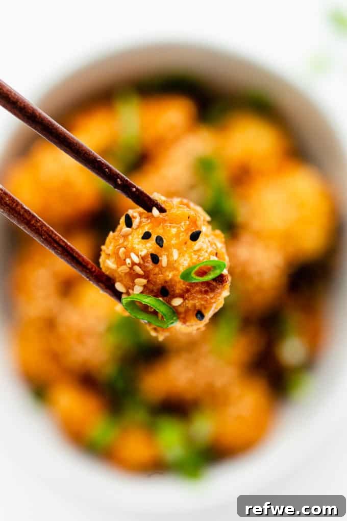 Sunkissed Cauliflower 11 A single piece of perfectly coated and baked orange cauliflower being held elegantly by chopsticks, showcasing its crispy texture.