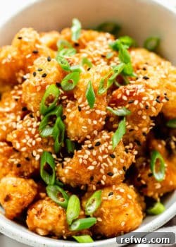 Crispy baked orange cauliflower topped with fresh sesame seeds and vibrant green scallions, ready to be served.