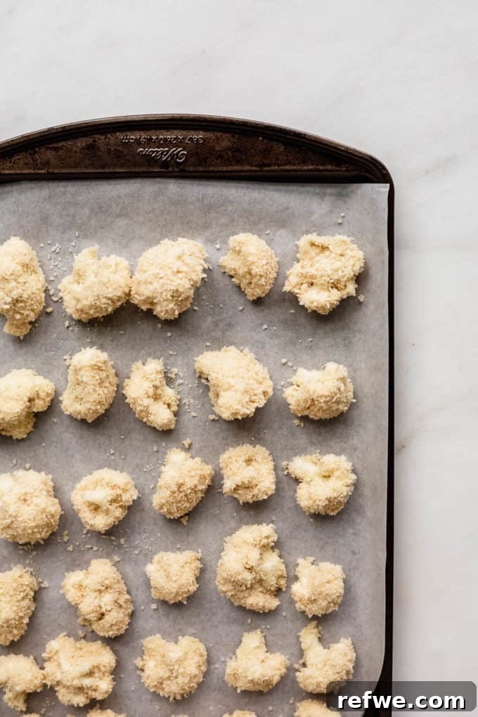 Sunkissed Cauliflower 6 Rows of panko-crusted cauliflower florets arranged neatly on a parchment-lined baking sheet, unbaked and ready for the oven.