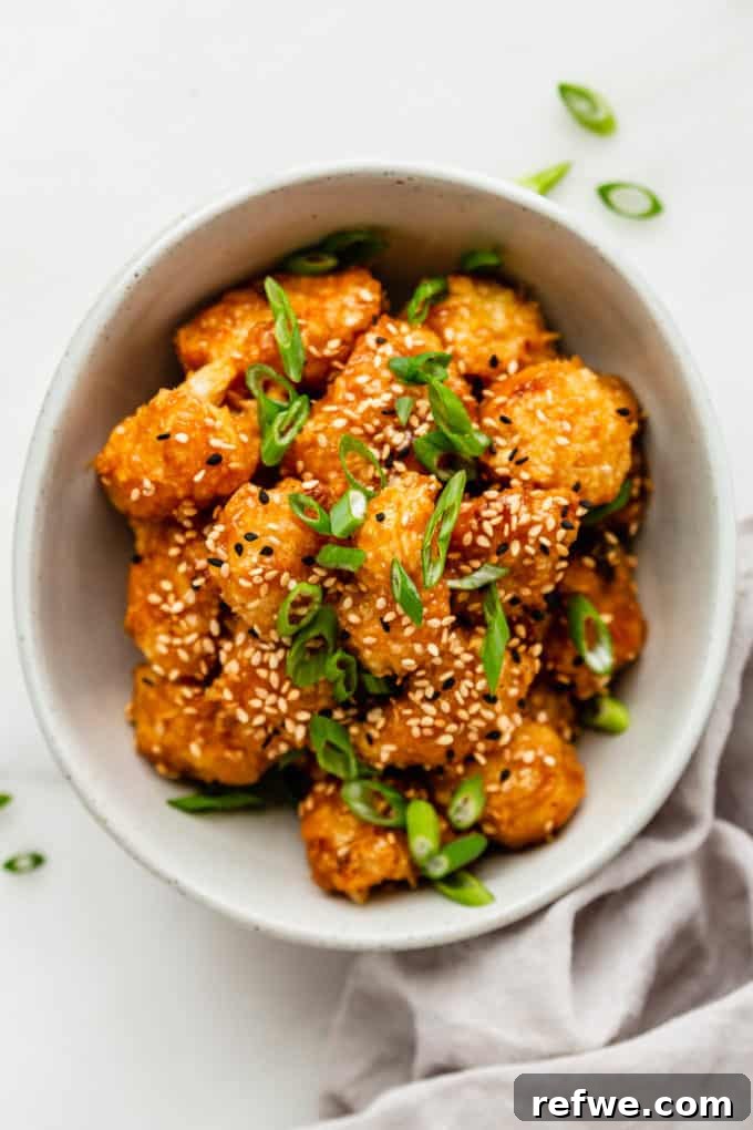 Sunkissed Cauliflower 9 A vibrant bowl of freshly prepared Orange Cauliflower, garnished with sesame seeds and chopped scallions, ready to be enjoyed.