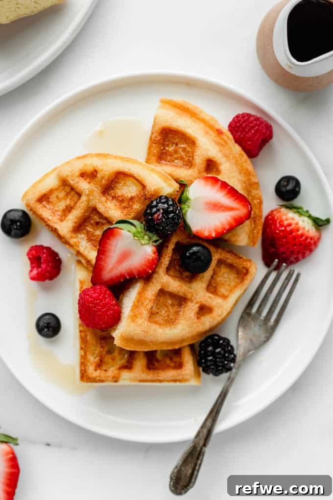 Fluffy Almond Flour Waffles 3 Two golden brown almond flour waffles stacked on a white plate, with a small pitcher of maple syrup to the side, ready to be poured.