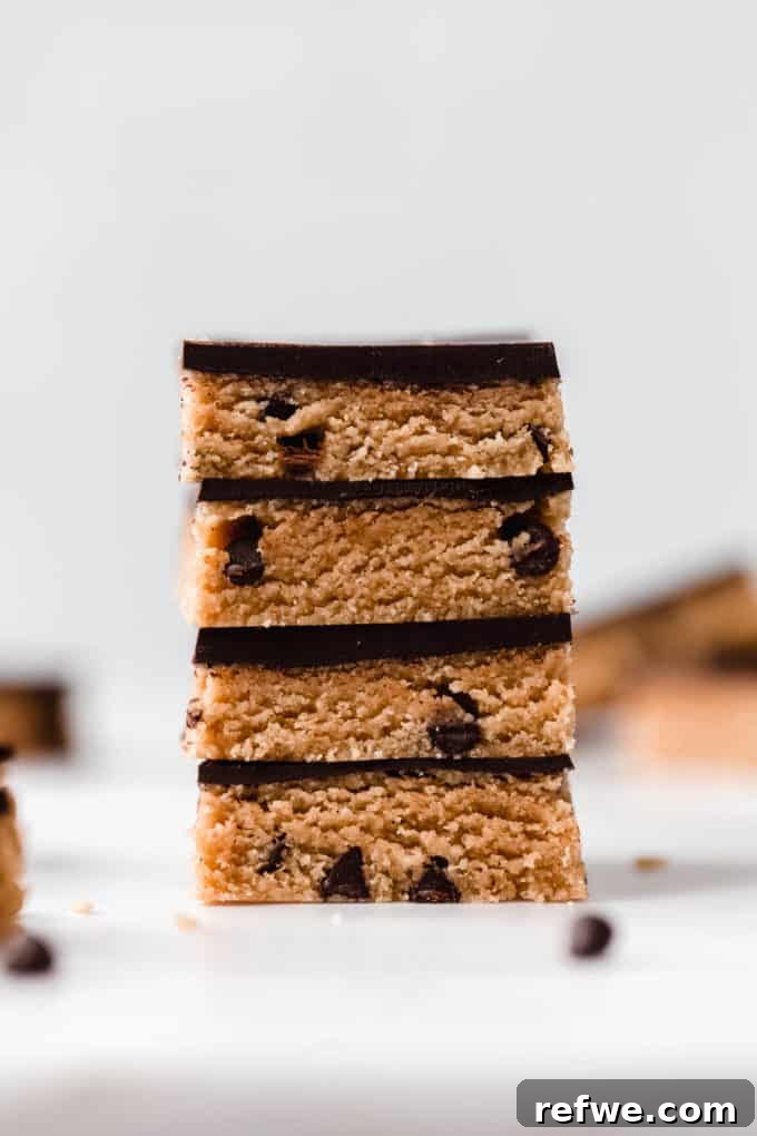 Fırınsız Sağlıklı Kurabiye Hamuru Barları 11 A striking stack of four healthy no-bake cookie dough bars, each featuring a thick, delicious chocolate topping and a rich, chewy cookie dough base.