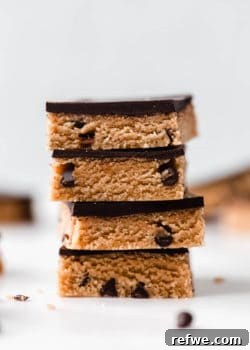 A stack of cookie dough bars topped with dark chocolate, showcasing the delicious layers.