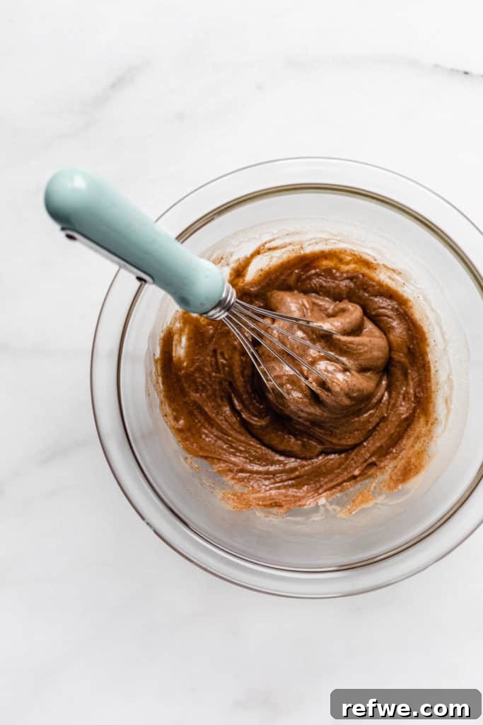 Fırınsız Sağlıklı Kurabiye Hamuru Barları 4 Creamy cashew butter blends with sweet maple syrup and extracts in a clear mixing bowl, being whisked to perfection for the wet ingredients.