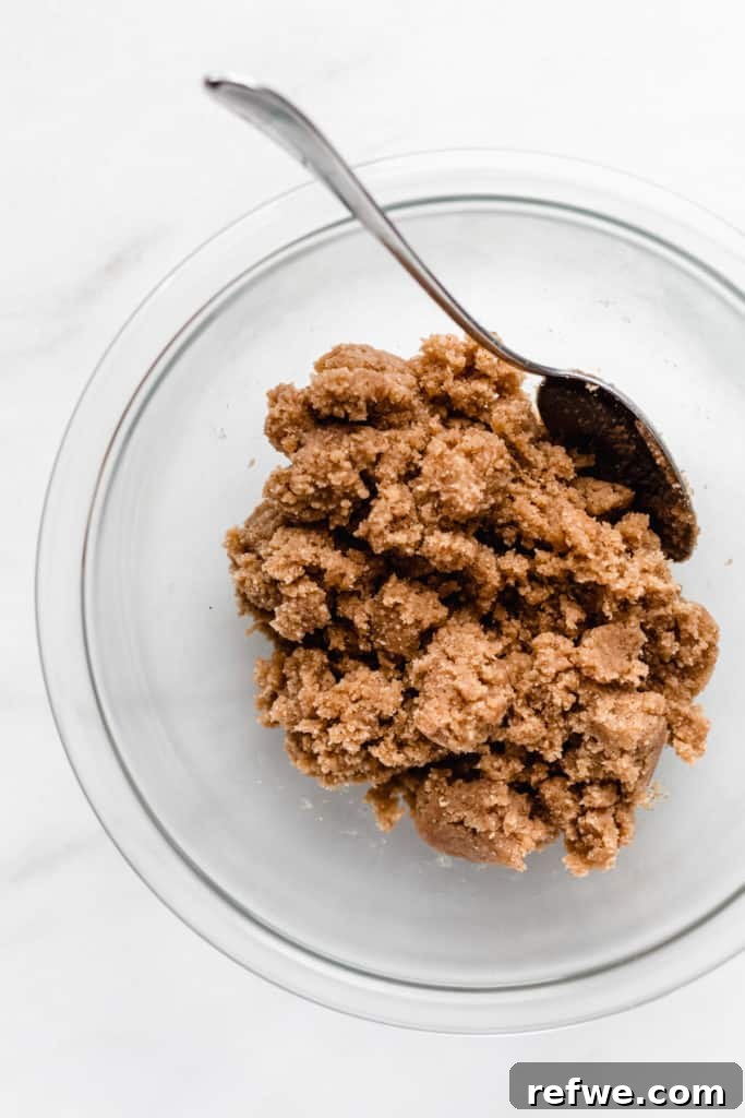 Fırınsız Sağlıklı Kurabiye Hamuru Barları 5 Almond flour cookie dough, partially mixed, rests in a clear bowl with a spoon, beginning to take shape.