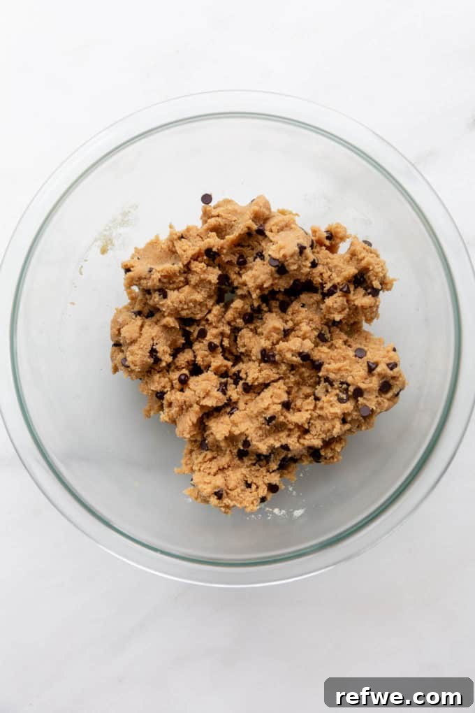 Fırınsız Sağlıklı Kurabiye Hamuru Barları 6 A perfectly mixed batch of no-bake cookie dough, studded with mini chocolate chips, is showcased in a clear glass mixing bowl.