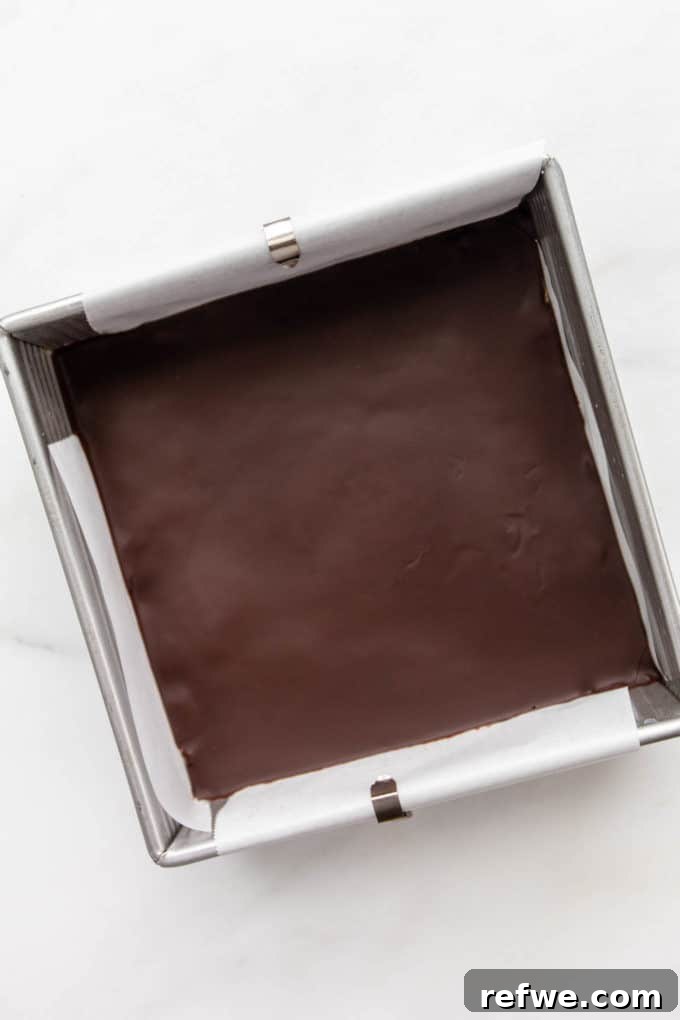 Fırınsız Sağlıklı Kurabiye Hamuru Barları 10 Perfectly set no-bake cookie dough bars with a glossy chocolate topping are showcased in an 8x8 inch pan, sliced and ready for serving.