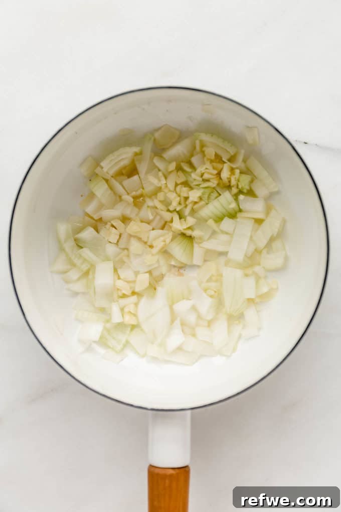 Velvety Vegan Broccoli Bliss 4 Chopped onion and garlic sizzling in olive oil in a white pot.