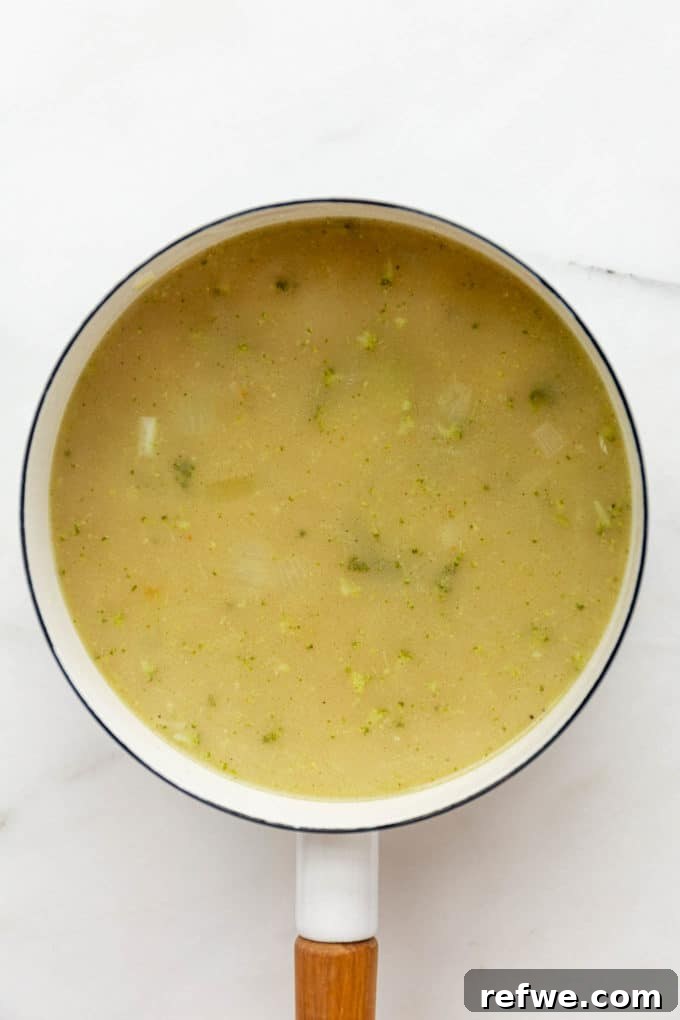 Velvety Vegan Broccoli Bliss 6 Creamy vegan broccoli soup being blended in a white pot with an immersion blender.