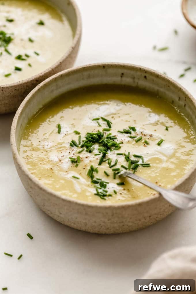 Velvety Vegan Broccoli Bliss 7 Creamy vegan broccoli soup in a bowl with a spoon, garnished with green herbs.