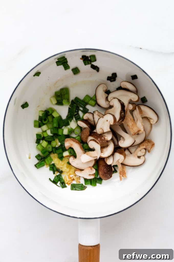 Whip Up Miso Ramen in 15 Minutes 6 Scallions, ginger, and shiitake mushrooms browning in a white pot, adding depth to the ramen broth.