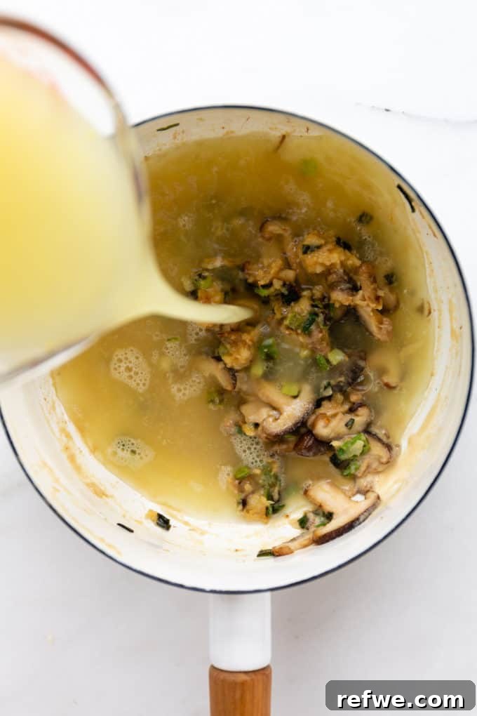 Whip Up Miso Ramen in 15 Minutes 8 Vegetable broth being poured into a white pot containing shiitake mushrooms, miso, and tahini, forming the ramen soup base.
