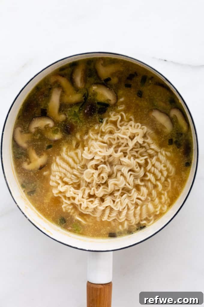 Whip Up Miso Ramen in 15 Minutes 10 Ramen noodles cooking in the miso ramen soup in a white pot, absorbing the rich flavors.