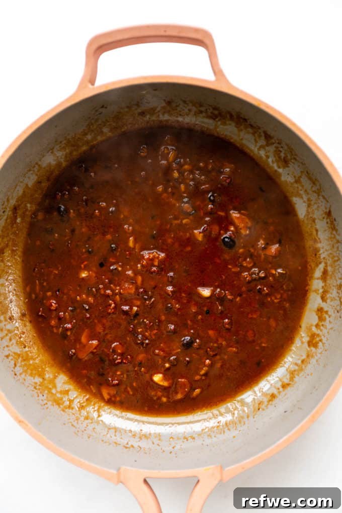 The vibrant red Mapo Tofu sauce simmering gently in a pink pan, thickening and intensifying its complex and aromatic flavors.
