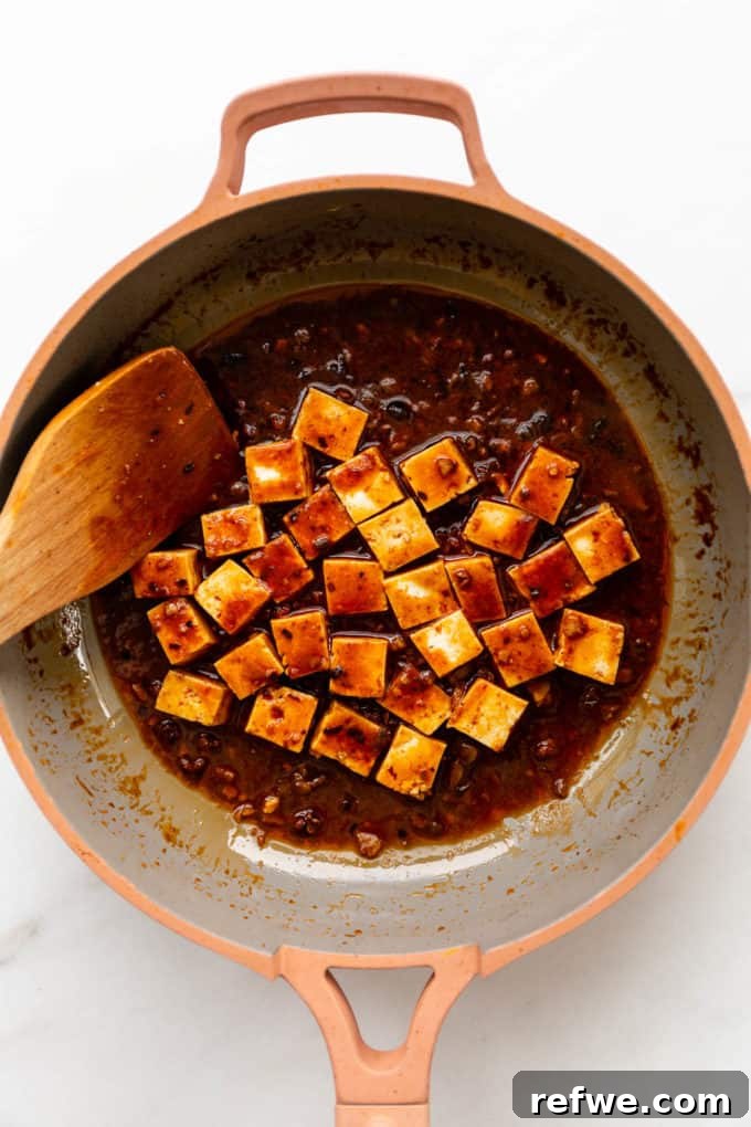 Soft tofu cubes gently mixed into the thick, red Mapo Tofu sauce in a pan, absorbing all the delicious and spicy flavors.