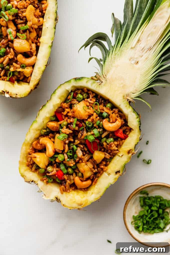 Pineapple Paradise Fried Rice 2 A stunning Thai Pineapple Fried Rice served elegantly in a hollowed-out pineapple half, garnished with fresh green onions and cilantro.