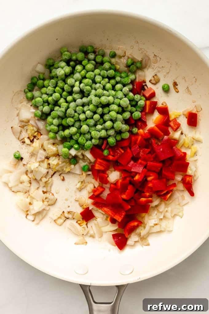 Pineapple Paradise Fried Rice 11 A colorful mix of onions, red bell peppers, and peas being sautéed in a white pan, perfectly prepped for fried rice.