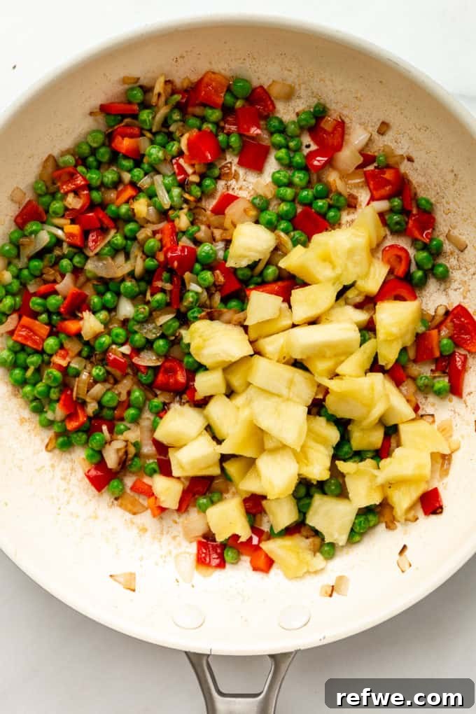 Pineapple Paradise Fried Rice 12 A vibrant medley of peas, red peppers, and pineapple pieces ready to be combined with rice in a white pan.