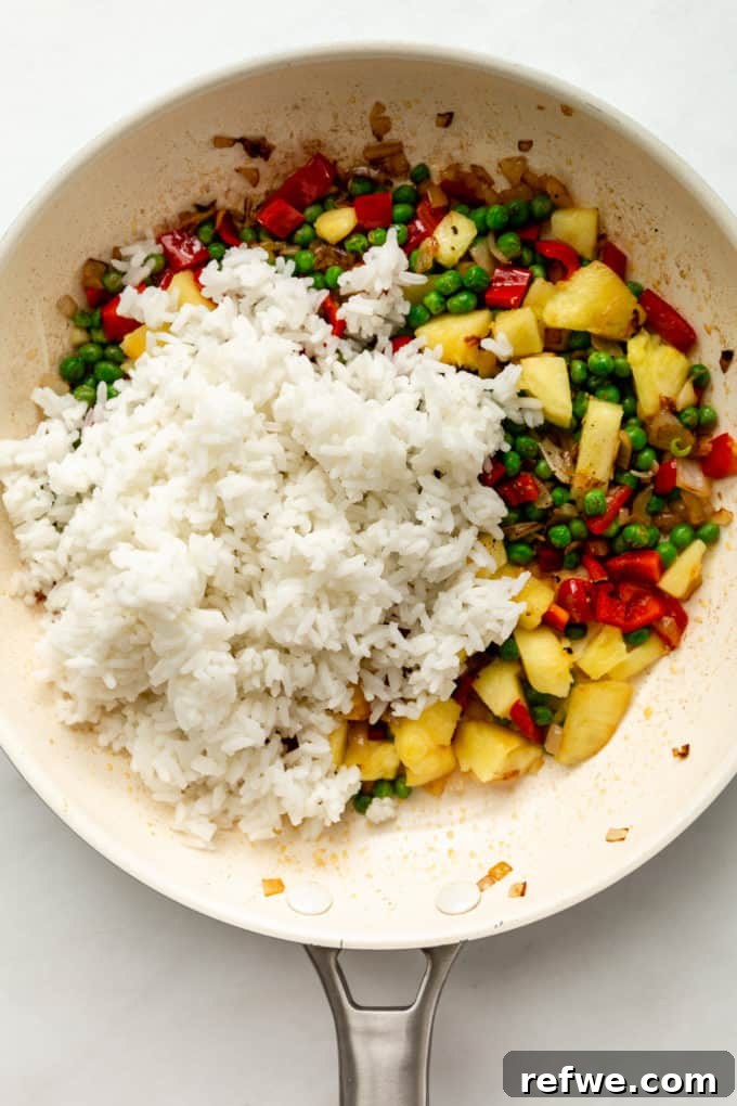 Pineapple Paradise Fried Rice 13 The harmonious blend of pineapple, colorful vegetables, and rice being stir-fried in a white pan, absorbing the delicious sauces.