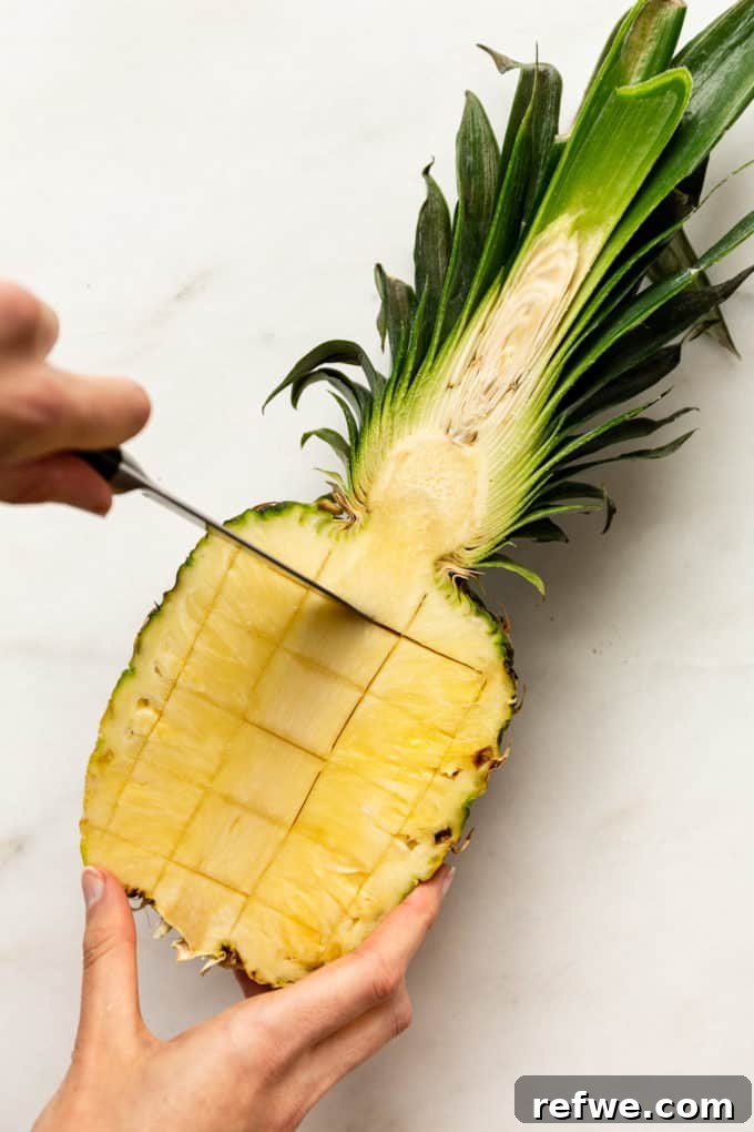 Pineapple Paradise Fried Rice 6 A knife making precise horizontal cuts in the pineapple half, demonstrating the technique for easy fruit removal.