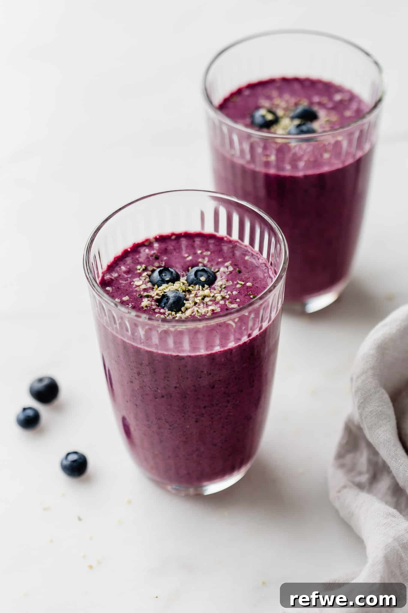 Vibrant Berry Spinach Blend 2 Two glasses of blueberry spinach smoothie topped with hemp seeds and blueberries, ready to be enjoyed.