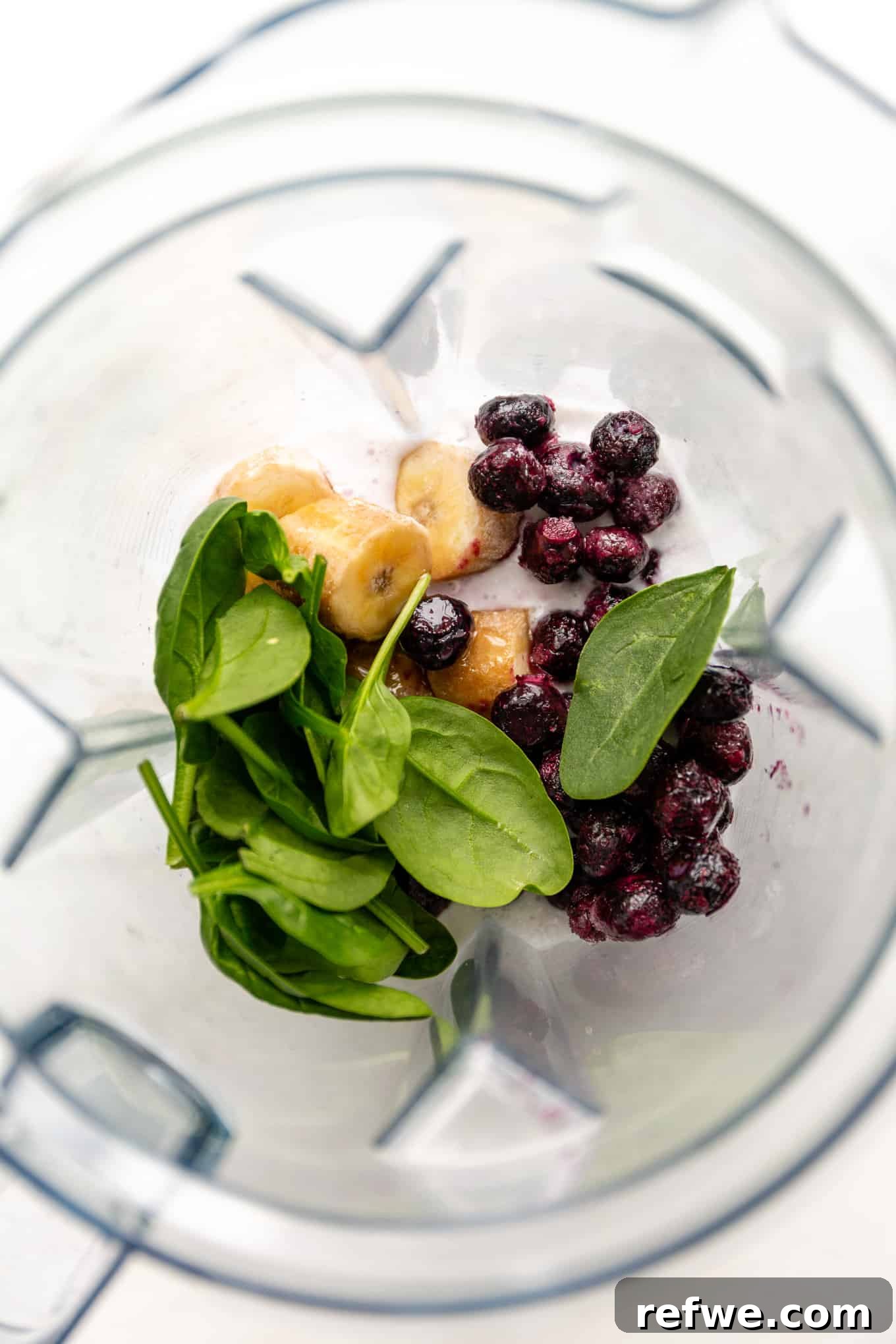 Vibrant Berry Spinach Blend 4 Blueberries, banana slices, and fresh spinach being added into a blender jar.