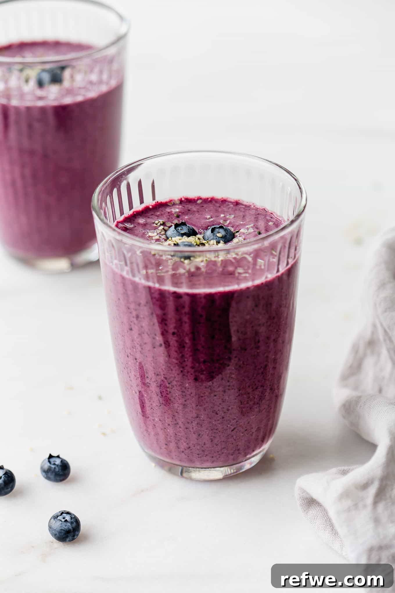 Vibrant Berry Spinach Blend 6 Two glasses of blueberry spinach smoothie with a grey napkin on the side, ready to be served.