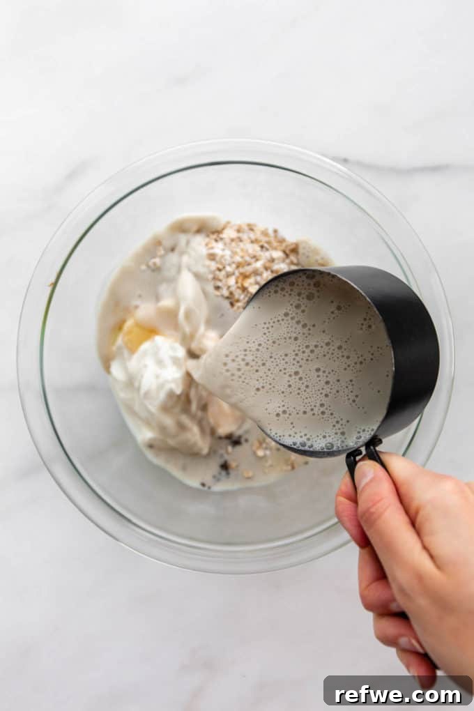 Power Protein Overnight Oats 6 A measuring cup pouring oat milk into a bowl of oats and other ingredients.