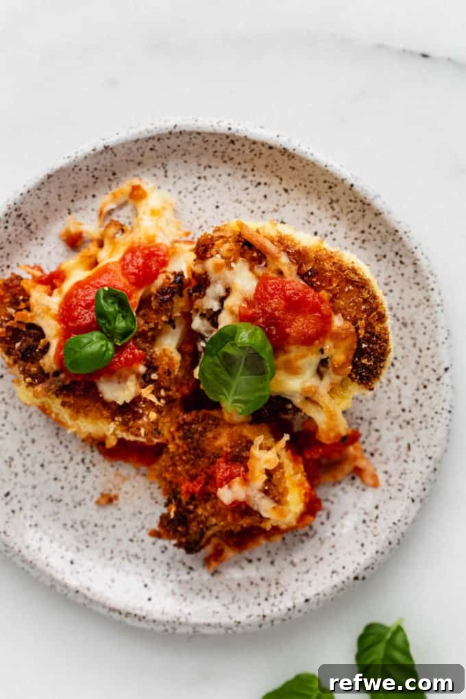 Golden Cauliflower Parmesan Bake 9 A vibrant close-up of Cauliflower Parmesan served on a white speckled plate, garnished with basil
