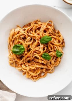 A bowl of red pesto pasta topped with fresh basil leaves