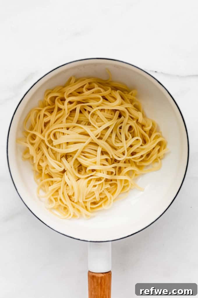 Velvety Red Pesto Pasta 5 Fettuccine pasta simmering in a white pot of boiling, salted water, illustrating the cooking process.