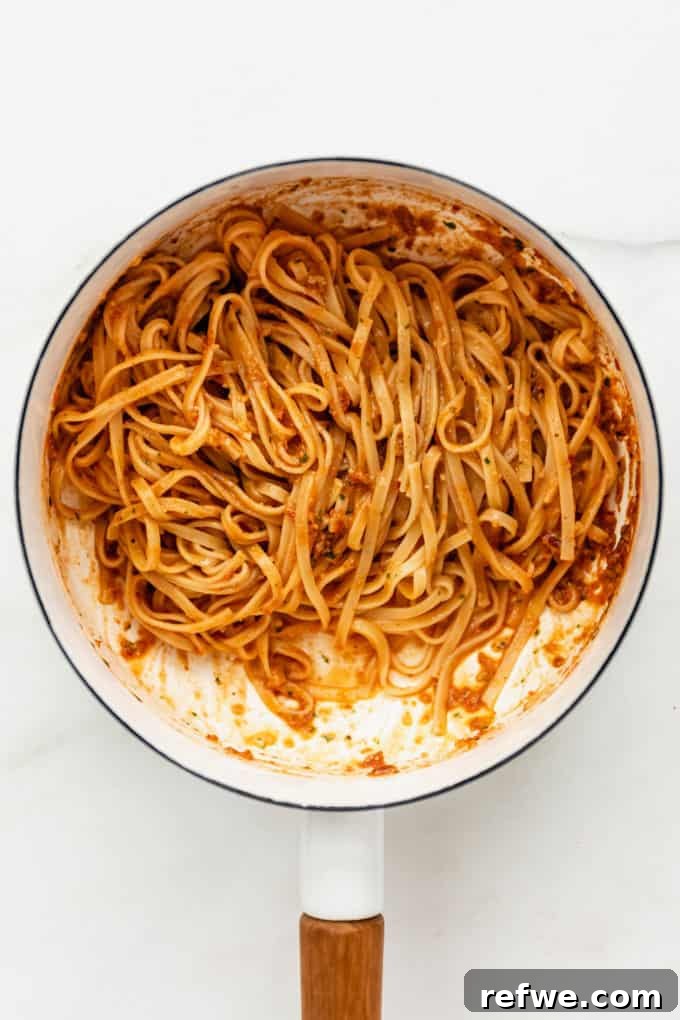 Velvety Red Pesto Pasta 7 Red pesto pasta being mixed in a white pot, with the vibrant sauce coating every strand beautifully and evenly.