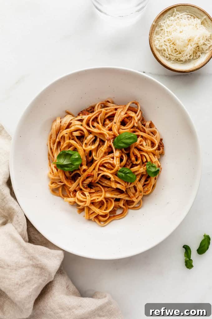 Velvety Red Pesto Pasta 8 A delightful bowl of red pesto pasta, served with a decorative napkin and a small side dish of grated Parmesan cheese, ready for enjoyment.