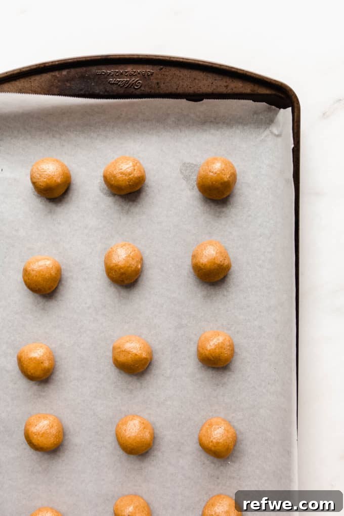 Irresistible Vegan Peanut Butter Treats 5 Small, perfectly rolled vegan peanut butter cookie dough balls arranged on a parchment-lined baking sheet.