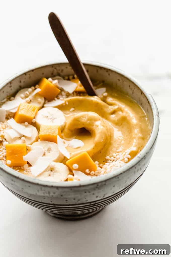 Golden Mango Bliss Bowl 6 A beautifully arranged mango smoothie bowl featuring sliced mango, fresh banana, and shredded coconut as toppings, photographed from an overhead perspective to showcase its vibrant colors and inviting texture.