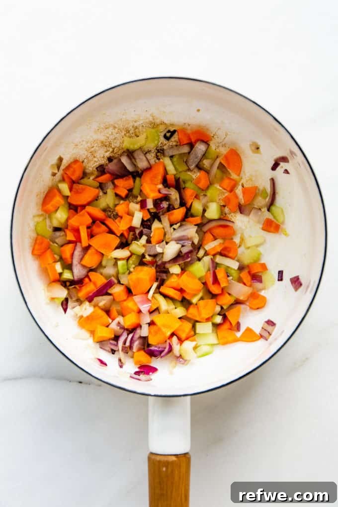 Creamy Vegan Corn Chowder 3 A white pot with carrots, celery and onions sautéing