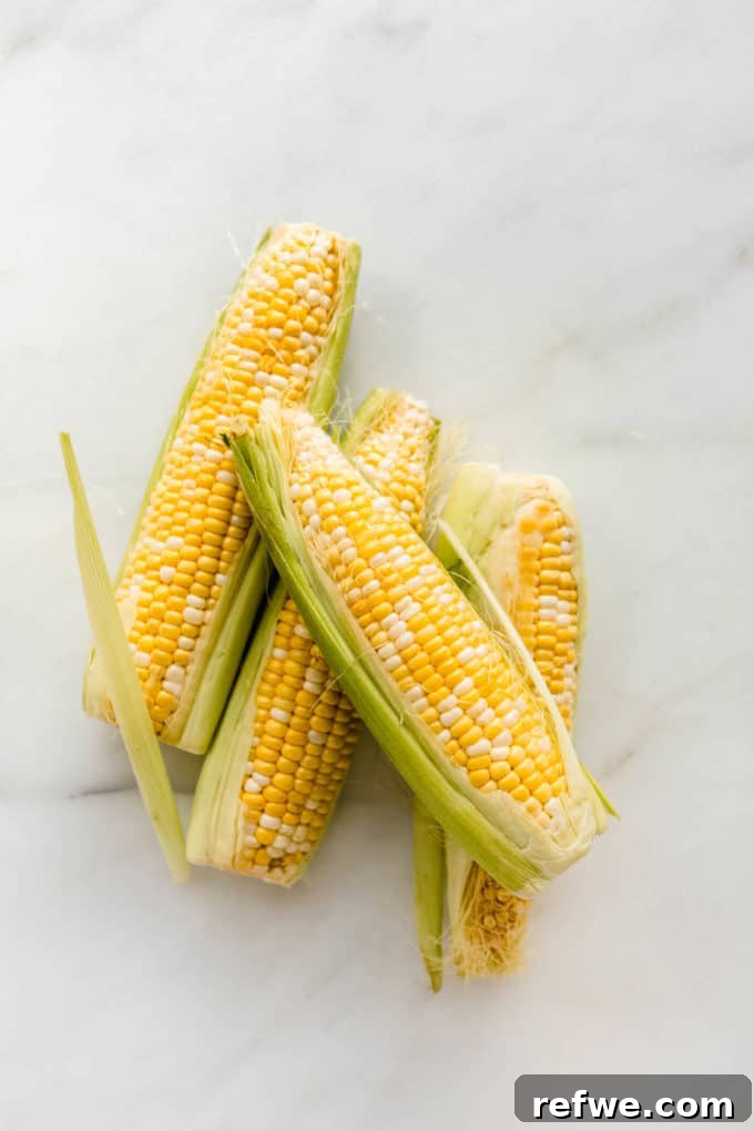 Creamy Vegan Corn Chowder 4 Four ears of fresh corn on a marble counter, ready to be prepared
