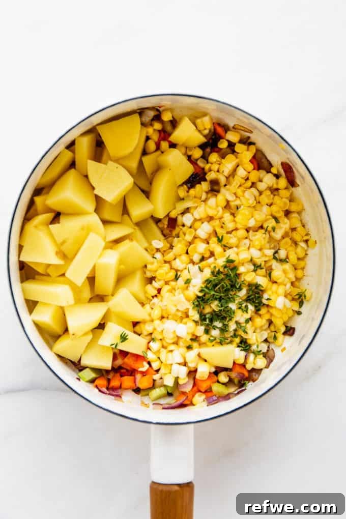 Creamy Vegan Corn Chowder 5 A white pot with potatoes, corn, and fresh thyme, ready for broth