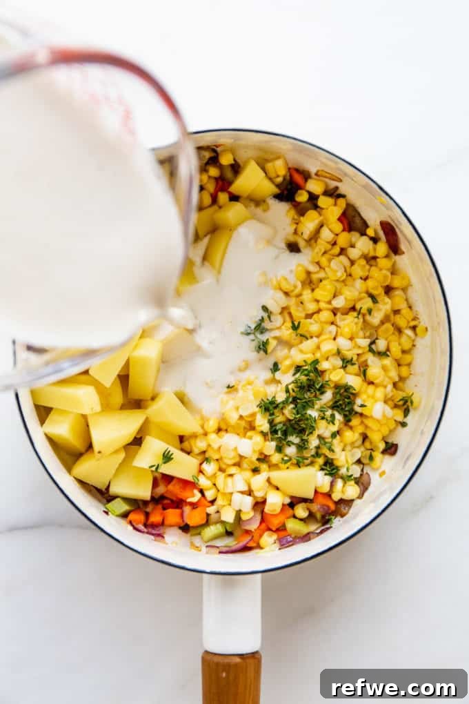 Creamy Vegan Corn Chowder 6 A measuring cup pouring smooth cashew cream into a pot of vegetables