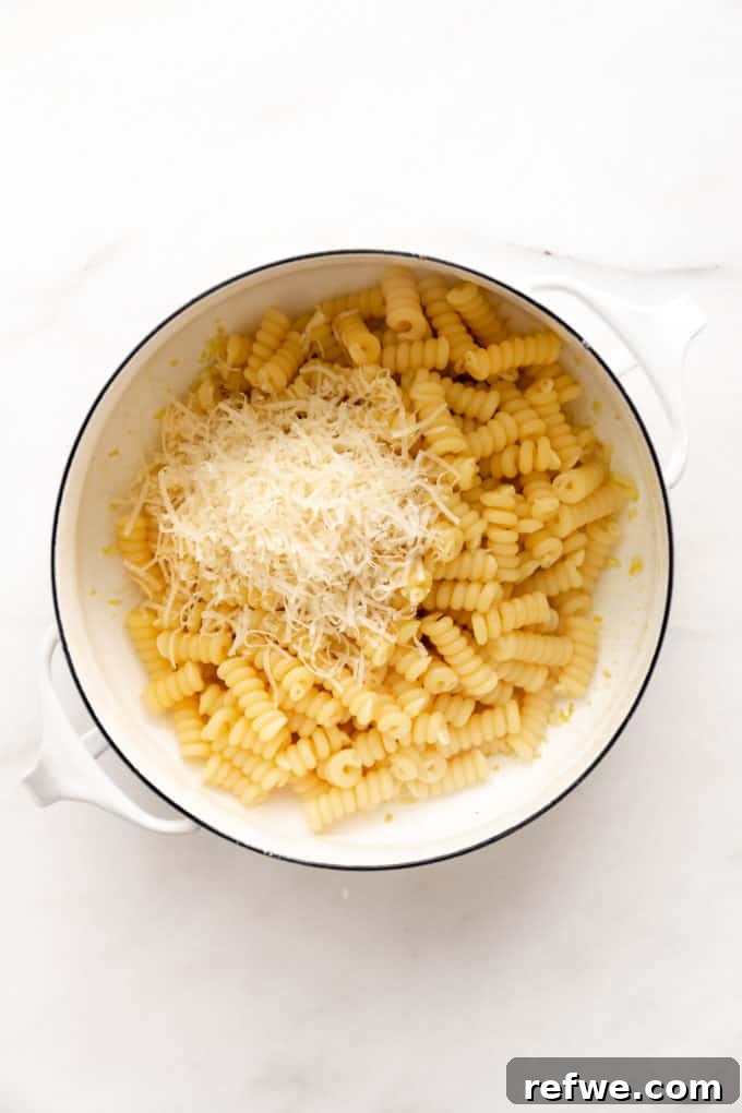 Zesty Lemon Garlic Pasta 6 Hot fusilli noodles and freshly grated parmesan cheese being added to a white pot with the lemon-garlic sauce